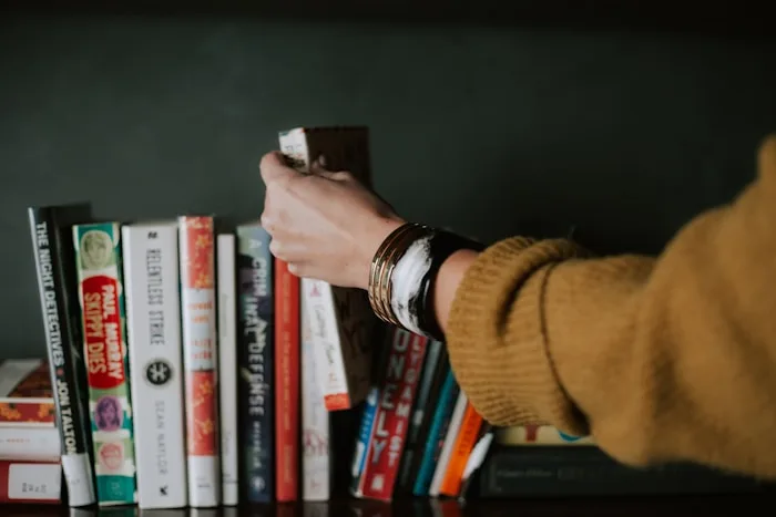 A hand reaches for a book on a shelf filled with titles, showcasing creative arts inspiration.