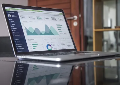 A laptop screen shows a data analytics dashboard with charts and metrics relevant to creative arts.