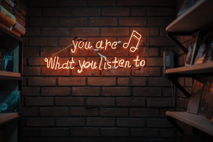 A brick wall showcases a neon sign with the quote 'you are What you listen to' and shelves displaying vinyl records.