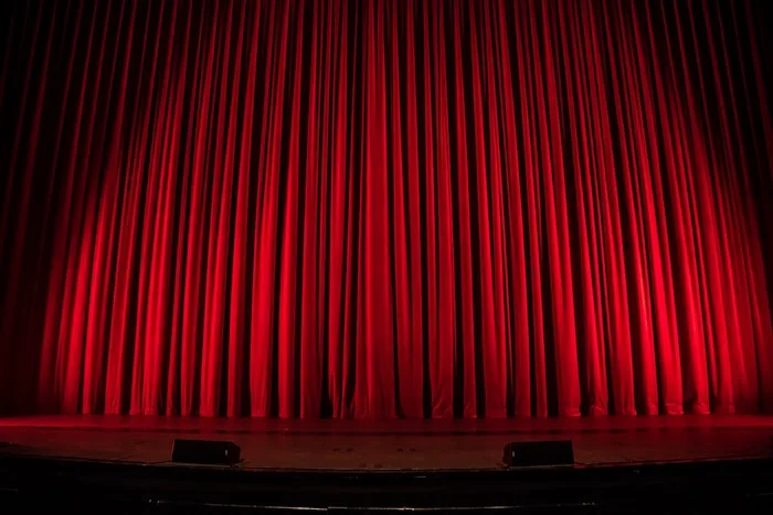 A red stage curtain suggests performing arts training at CAQA Creative.