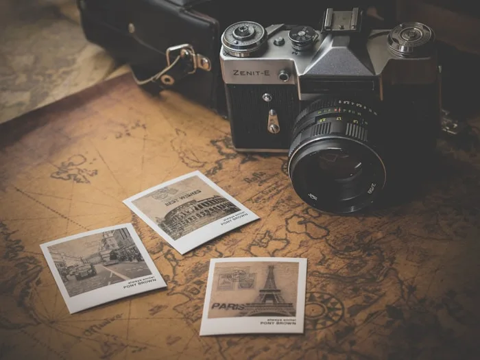 A vintage Zenit-E camera sits on a map covered with travel photos from Paris and Rome, representing visual arts.